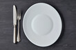 © OneBit - Oval white plate on a dark concrete background with cutlery