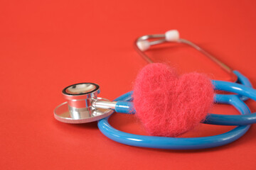 Wall Mural - heart made of wool and a medical stethoscope on a bright red background