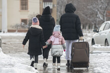 A Family Of Four With A Dog Leaves The City For A Trip And Walks Along The Road With A Large Suitcase In The Winter Season Through The Snow