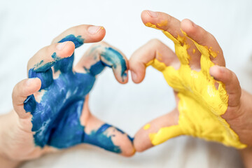 Children's hands painted in blue and yellow color in heart shape, flag of Ukraine. Stop war symbol. Ukrainian Independence Flag Day.