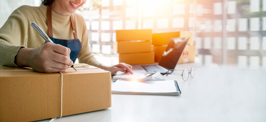 Young woman small business owner writing on parcel box preparing package product for her customer. SME entrepreneur or freelance life style concept.