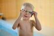 © ninelutsk - Happy cute toddler child near the pool side smiling in goggles after swimming lesson indoor. Physical development and healthy water activities for kids