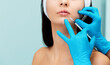 © _KUBE_ - Woman on a lip augmentation procedure. A beautician in blue rubber gloves gives an injection to the lower lip. Results before and after procedure. Copy space. Concept of professional cosmetology