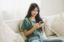 Happy Young Asian Woman Relaxing At Home She Is Sitting On Sofa And Using Mobile Smartphone