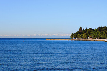 Wall Mural - Wonderful view of the snow covered Alps mountains against blue Adriatic Sea and sky in winter holidays. Slovenia, Strunjan