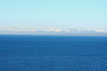 Wall Mural - Wonderful view of the snow covered Alps mountains against blue Adriatic Sea and sky in winter holidays. Slovenia, Strunjan