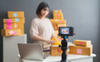 © sutthinon602 - Beautiful asian woman blogger showing clothes in front of camera to recording vlog video live streaming at her shop. Business online influencer on social media concept. Online Selling. Online Shopping