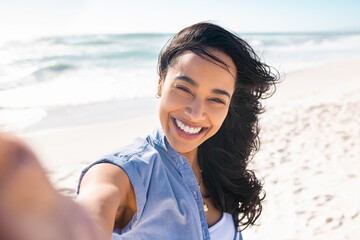 Wall Mural - Laughing latin woman on beach taking selfie during summer vacation