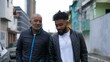 © Marco - An African father and adult son walking together outside in urban street two people bonding