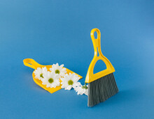 Yellow Dustpan And Brush With White Marguerite Daisies Flowers On Blue Background.