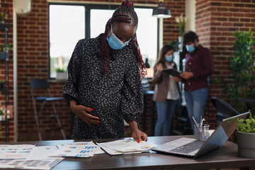Wall Mural - pregnant african american businesswoman using work laptop to review marketing strategy and proposed 