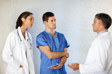 Canvas Print - Theyre in the business of saving lives. A cropped shot of three doctors standing and having a serious conversation.