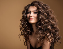 Curly Hair Model. Woman Wavy Long Hairstyle. Brunette Fashion Girl With Volume Hairdo And Natural Make Up Over Beige Background
