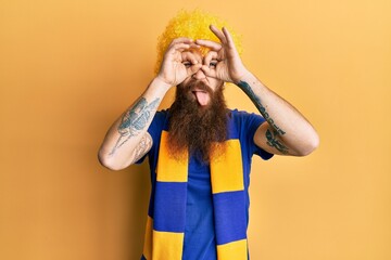 Sticker - Redhead man with long beard football hooligan cheering game wearing funny wig doing ok gesture like binoculars sticking tongue out, eyes looking through fingers. crazy expression.