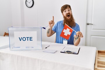 Canvas Print - Caucasian man with long beard at political campaign election holding swiss flag surprised with an idea or question pointing finger with happy face, number one