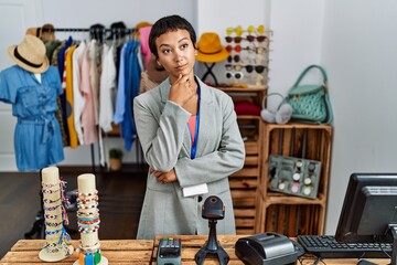 Poster - Young hispanic woman with short hair working as manager at retail boutique looking confident at the camera smiling with crossed arms and hand raised on chin. thinking positive.