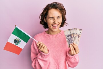 Poster - Young brunette woman holding mexico flag and mexican pesos banknotes winking looking at the camera with sexy expression, cheerful and happy face.