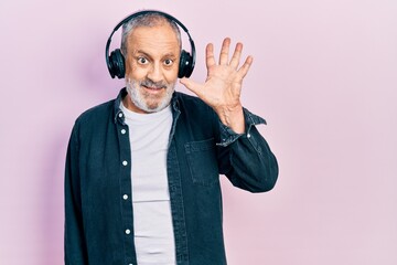 Canvas Print - Handsome senior man with beard listening to music using headphones showing and pointing up with fingers number five while smiling confident and happy.