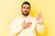 © Asier - Young caucasian man isolated on yellow background taking an oath, putting hand on chest.