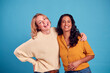 Portrait Of Two Mature Female Friends Laughing At Camera Against Blue Background