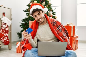 Poster - Young hispanic man wearing christmas hat using laptop and credit card at home.