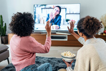Women Waving Hands On Video Call With Friend Through Television Set At Home