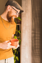 Cheerful Man Holding Coffee Cup Standing By Window At Home