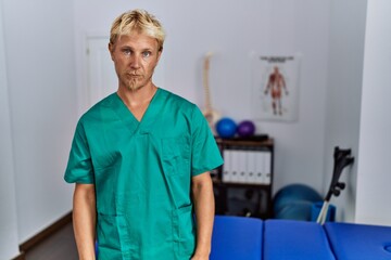 Poster - Young blond man wearing physiotherapist uniform standing at clinic depressed and worry for distress, crying angry and afraid. sad expression.