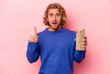 Wall Mural - Young caucasian man holding chickpeas isolated on pink background having some great idea, concept of creativity.