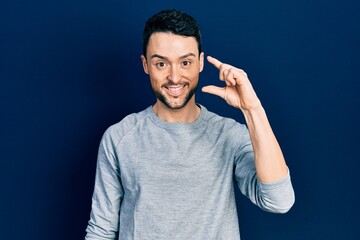 Poster - Young hispanic man wearing casual clothes smiling and confident gesturing with hand doing small size sign with fingers looking and the camera. measure concept.