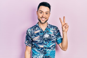 Poster - Young hispanic man wearing casual clothes smiling with happy face winking at the camera doing victory sign. number two.