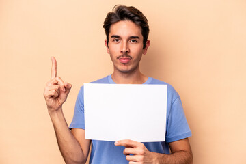 Young caucasian man holding a placard isolated on beige background showing number one with finger.