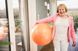 © Westend61 - Happy woman with fitness ball standing at glass window at home