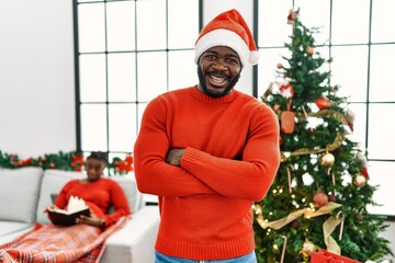 Sticker - Young african american man standing by christmas tree happy face smiling with crossed arms looking at the camera. positive person.