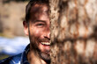 © Westend61 - Happy man behind tree truck on sunny day