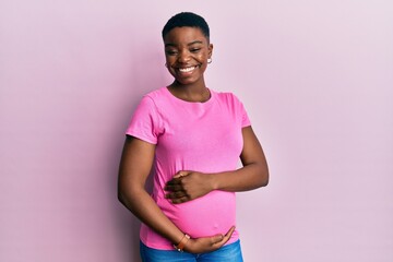 Wall Mural - Young african american woman expecting a baby, touching pregnant belly winking looking at the camera with sexy expression, cheerful and happy face.