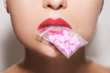 Wall Mural - Woman holding ziplock bag with pink pills in her mouth.