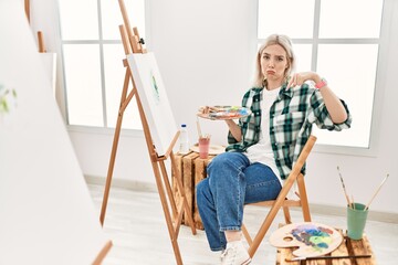 Poster - Young artist woman painting on canvas at art studio pointing down looking sad and upset, indicating direction with fingers, unhappy and depressed.