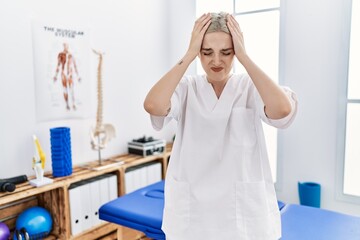 Sticker - Young caucasian woman working at pain recovery clinic suffering from headache desperate and stressed because pain and migraine. hands on head.