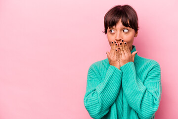 Wall Mural - Young hispanic woman isolated on pink background thoughtful looking to a copy space covering mouth with hand.