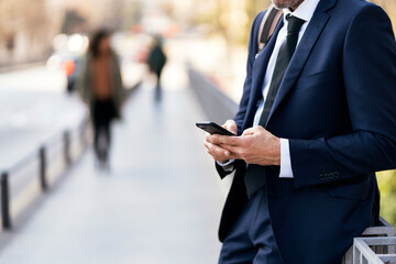 Crop businessman using smartphone on street