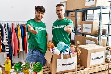 Poster - Young gay couple wearing volunteer t shirt at donations stand smiling cheerful offering palm hand giving assistance and acceptance.