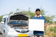 © WESTOCK - Smiling car mechanic showing white empty board or placard with spanner looking at camera - concept of promotion for mobile service and maintenance service advertisement