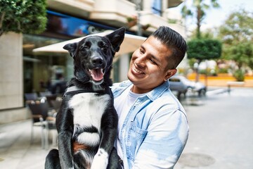 Canvas Print - Young latin man smiling happy holding dog at the city.