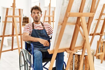 Sticker - Young handsome man with beard at art studio sitting on wheelchair scared and amazed with open mouth for surprise, disbelief face