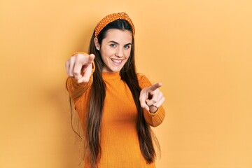 Young brunette teenager wearing casual yellow sweater pointing to you and the camera with fingers, smiling positive and cheerful