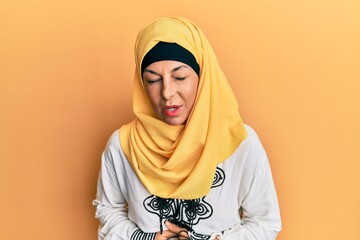 Sticker - Middle age hispanic woman wearing traditional islamic hijab scarf with hand on stomach because indigestion, painful illness feeling unwell. ache concept.