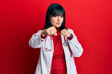 Poster - Young hispanic woman wearing doctor uniform and stethoscope punching fist to fight, aggressive and angry attack, threat and violence