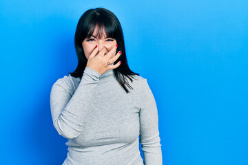 Canvas Print - Young hispanic woman wearing casual clothes smelling something stinky and disgusting, intolerable smell, holding breath with fingers on nose. bad smell