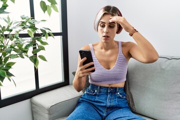 Canvas Print - Young beautiful woman using smartphone typing message sitting on the sofa worried and stressed about a problem with hand on forehead, nervous and anxious for crisis